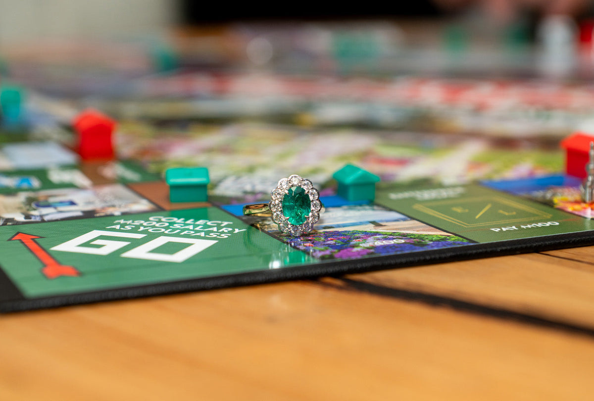 18k yellow and white gold cluster ring with oval cut natural emerald and natural round brilliant cut white diamonds on Toowoomba Monopoly board.