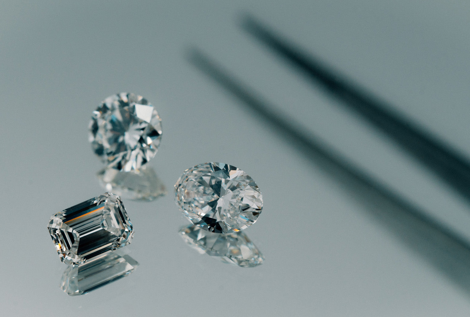 Emerald, oval and round brilliant cut natural white diamonds on a mirror background.