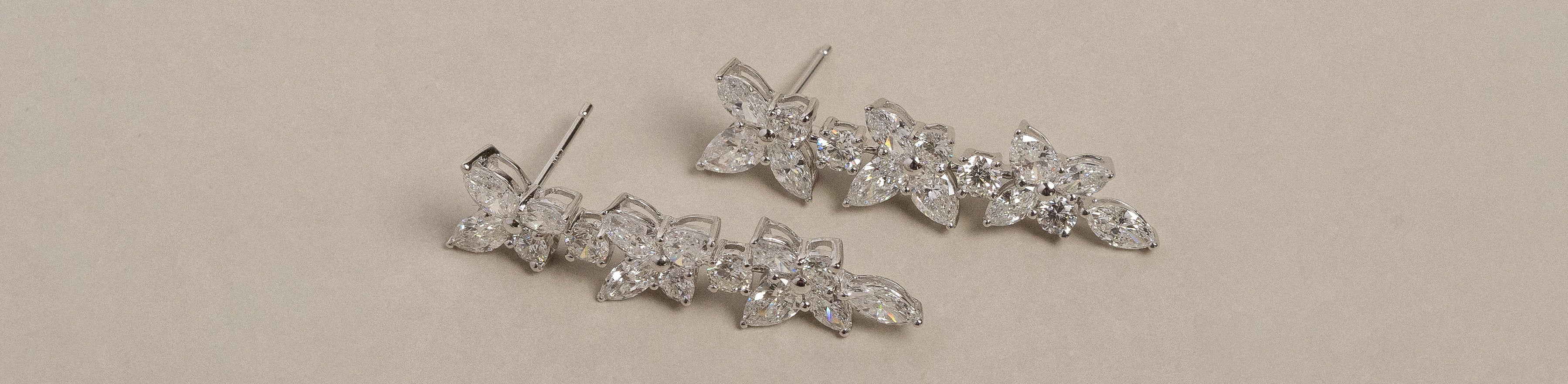 White gold diamond set drop earrings on a cream background.