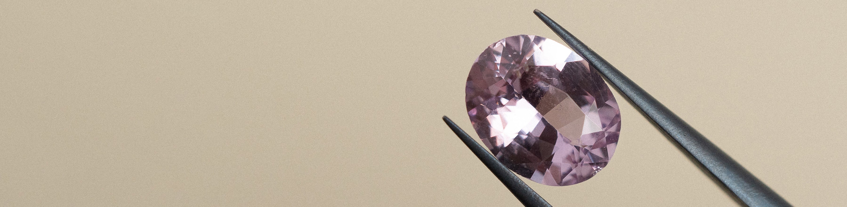 Oval cut amethyst gemstone in tweezers on a cream background.