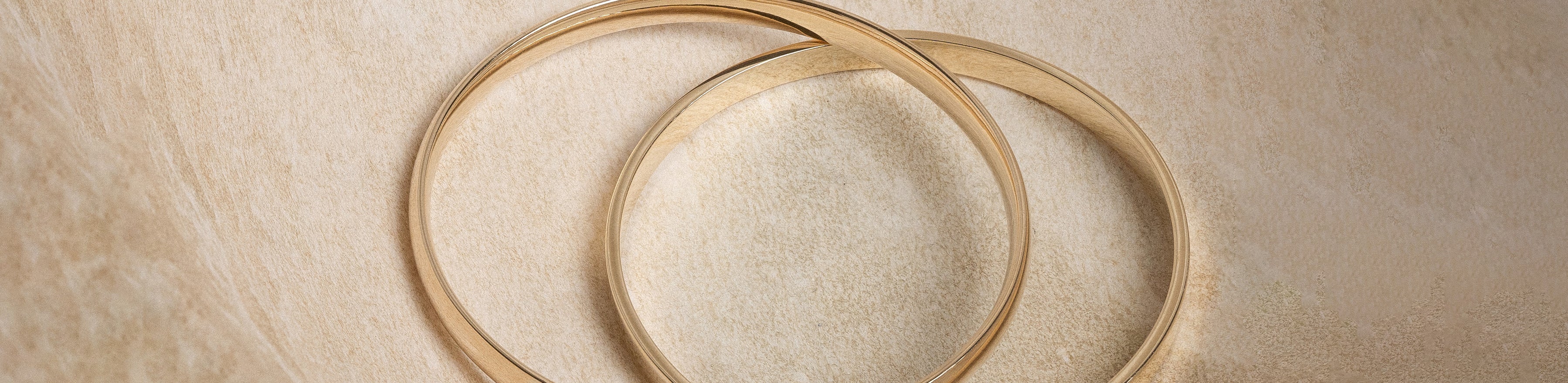 Yellow gold bangles on a travertine background.