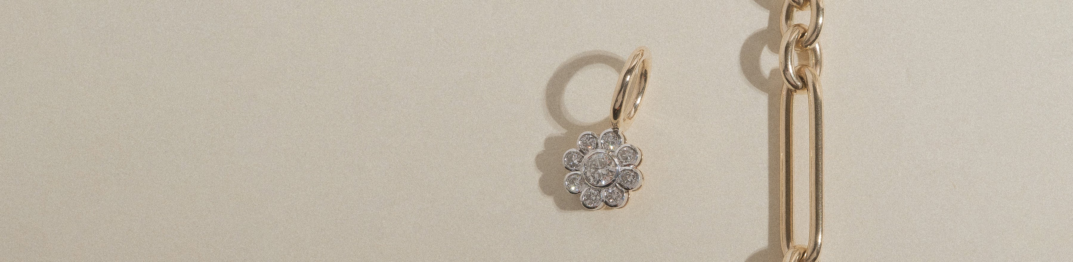 Yellow and white gold flower cluster diamond pendant with a paperclip chain on a cream background.