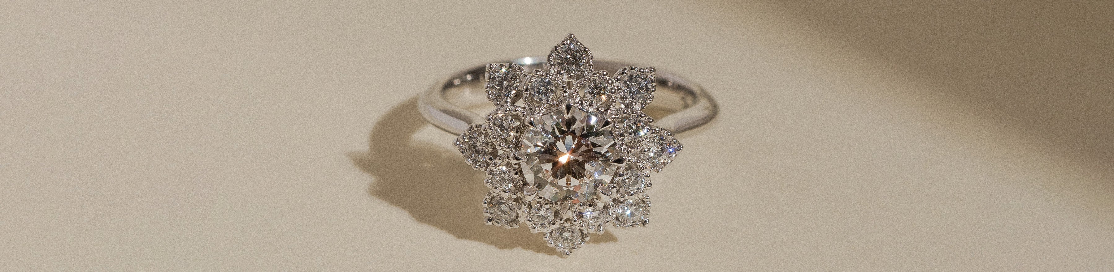 White gold round brilliant cut white diamond halo ring on a cream background.