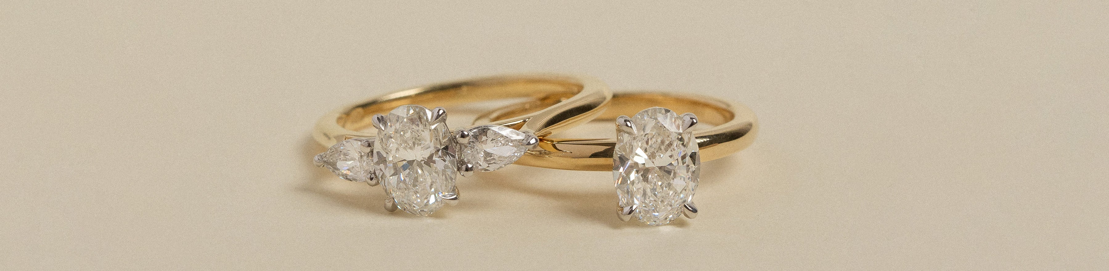 Solitaire oval and trilogy oval diamond rings on a cream background.