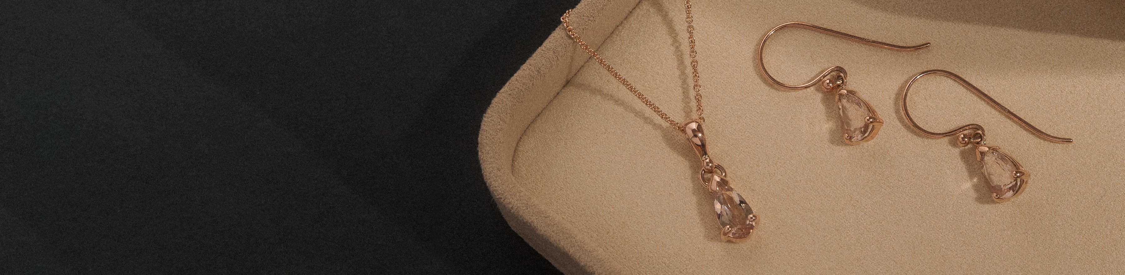 Rose gold pear cut morganite pendant and drop earring set in a cream box on a black background.