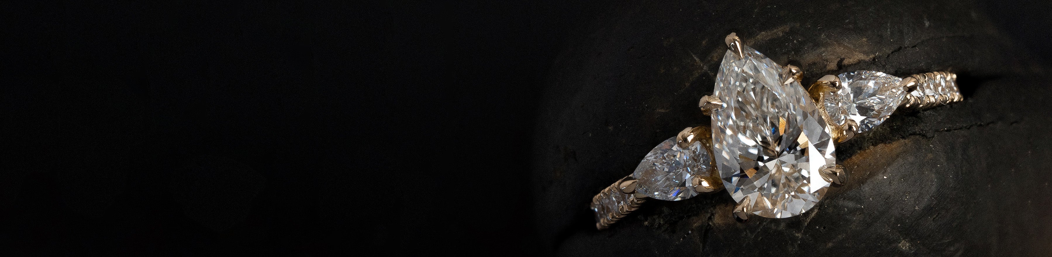 Yellow gold pear cut natural diamond trilogy ring on black background.