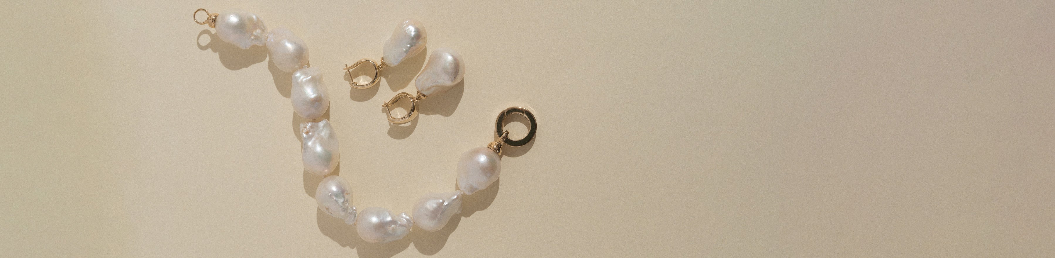 9k yellow gold and baroque pearl bracelet and earrings on a cream background.