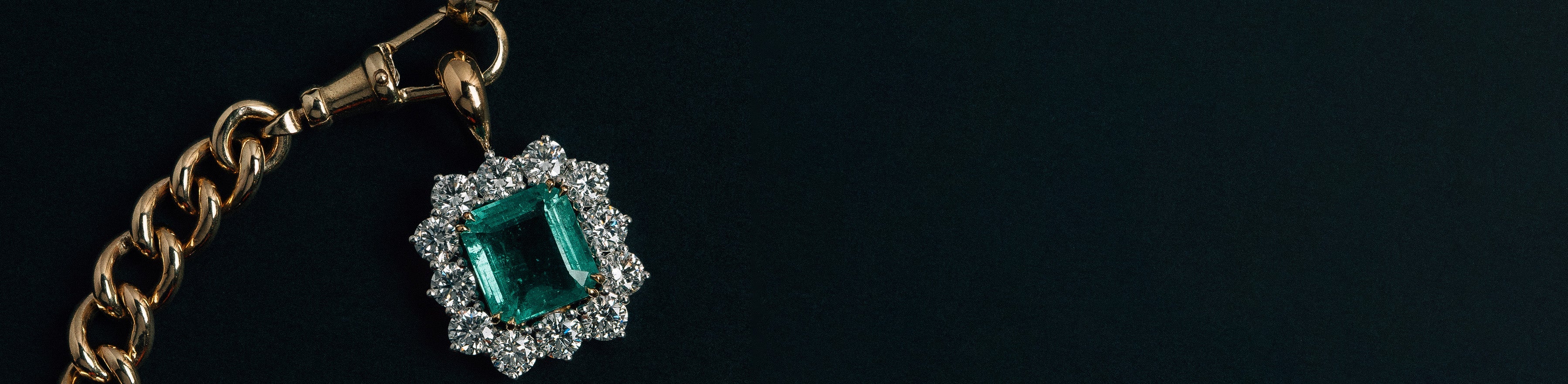 Yellow and white gold emerald gemstone and diamond cluster pendant on a thick gold curb chain, on a black background.