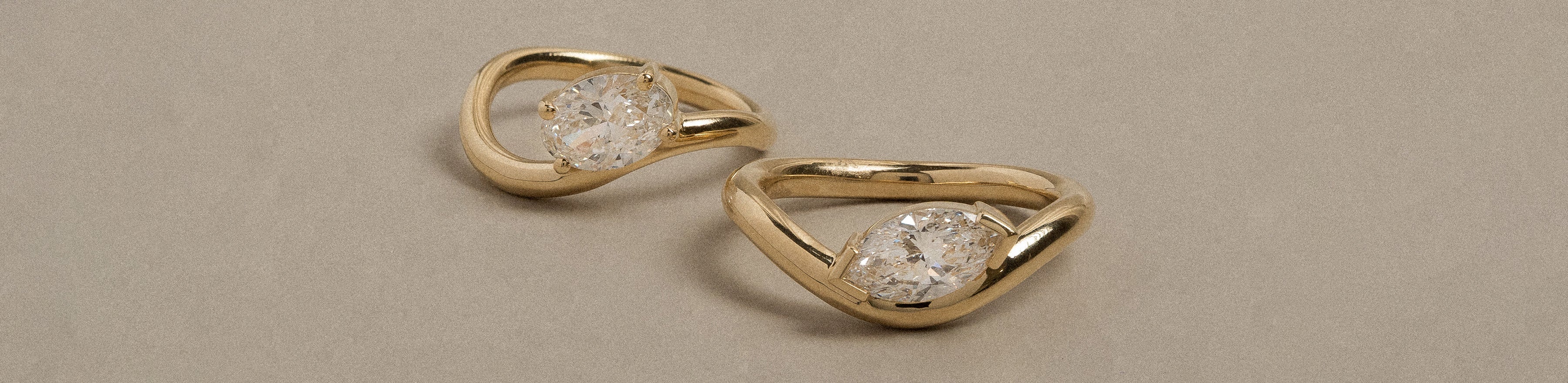 Contoured marquise and oval cut solitaire rings on a cream background.