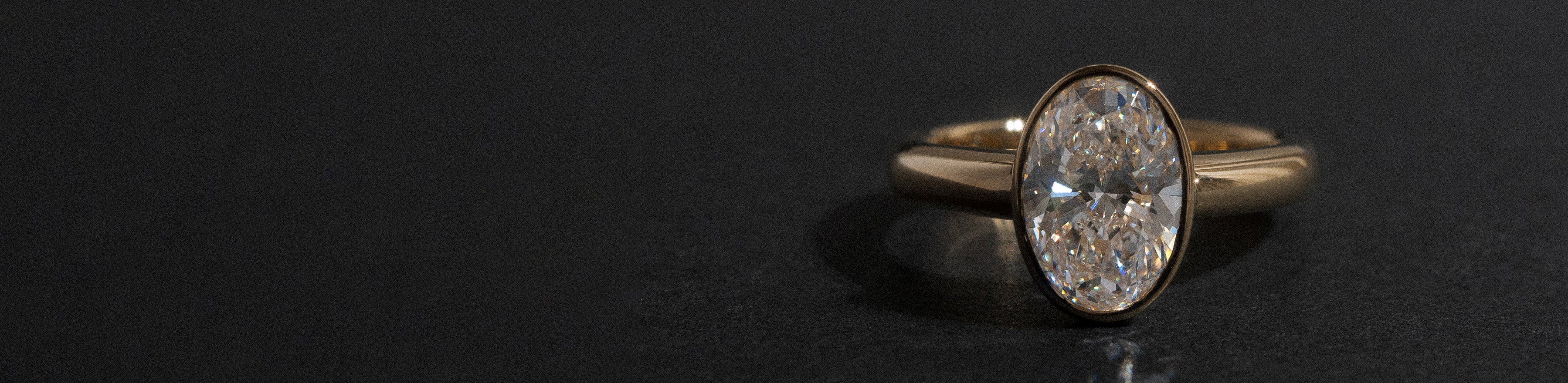 Yellow gold bezel set natural oval diamond ring on black background.