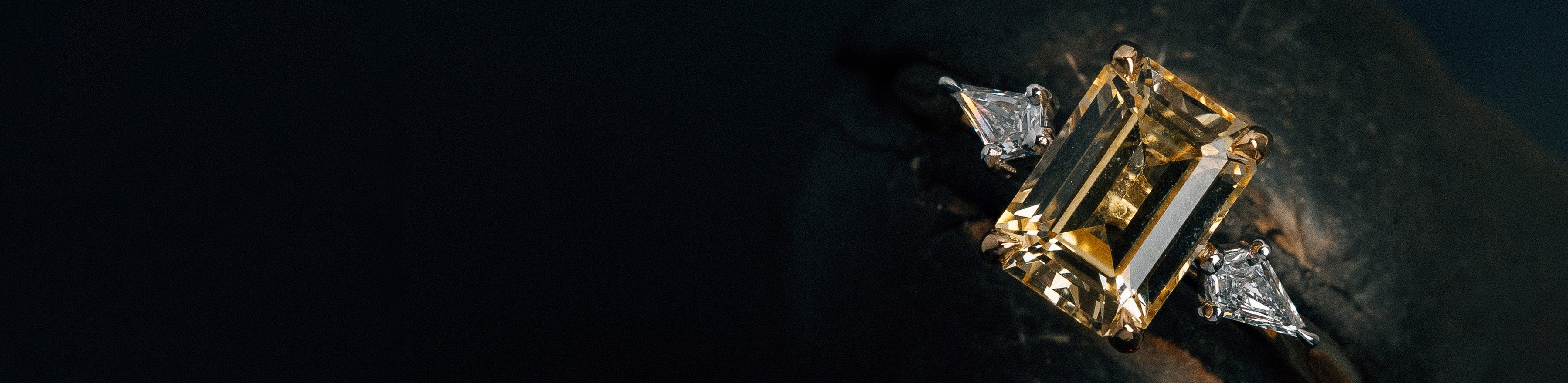 Yellow and white gold emerald cut yellow sapphire trilogy ring on a black background.