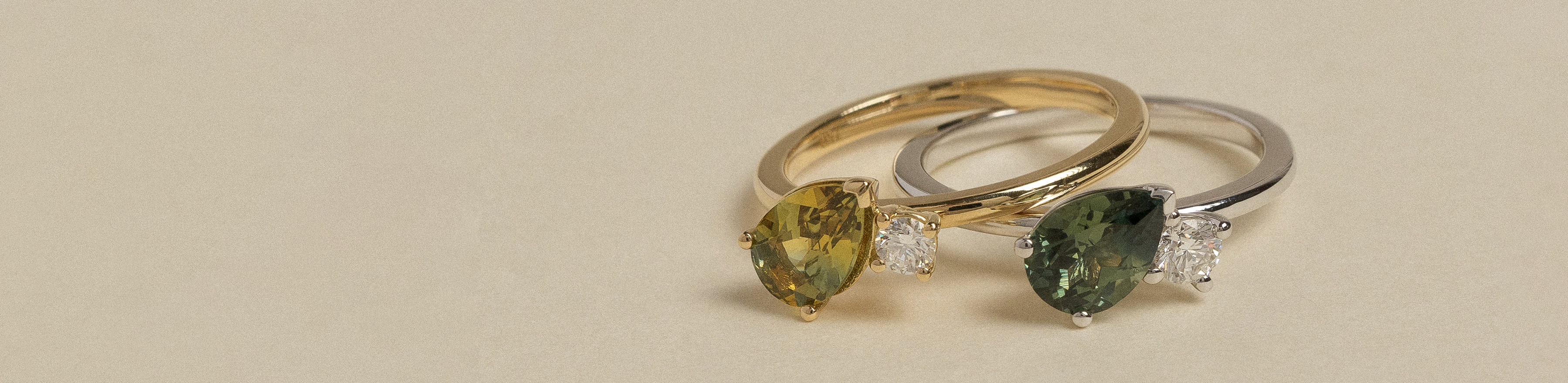 Yellow and white gold sapphire and diamond two stone rings on a cream background.