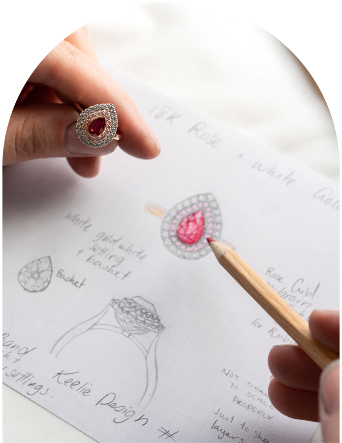 Jewellery designer's hand holding a ruby and diamond ring, whilst sketching a bespoke piece.