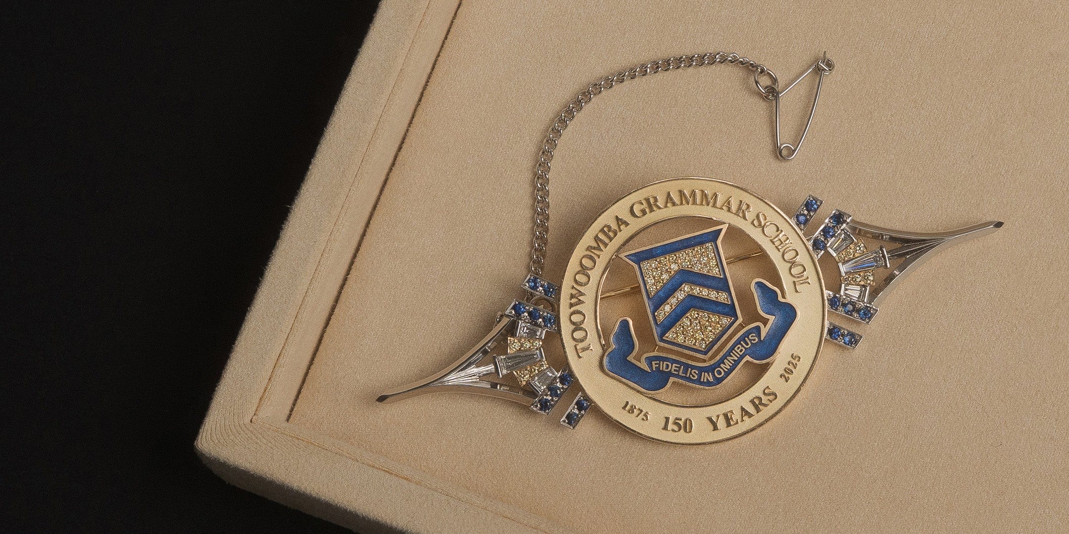 Custom made Toowoomba Grammar School brooch in beige pendant box on black background.