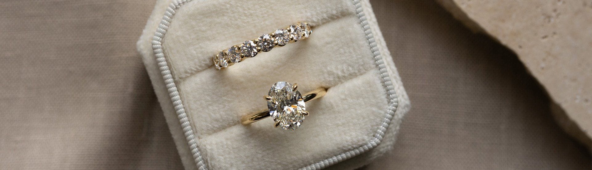 Yellow gold oval solitaire engagement ring and claw set diamond wedding ring in an octagonal velvet cream ring box.