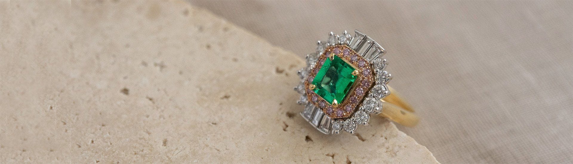 Handcrafted rose, white and yellow gold emerald and pink diamond cluster ring positioned on travertine.