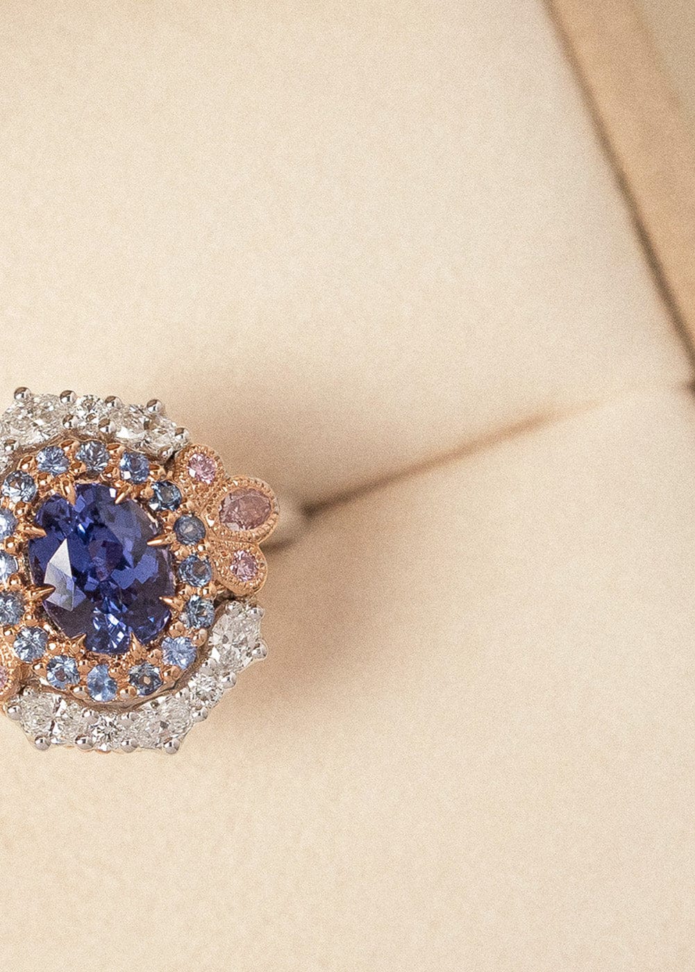 Bespoke oval cut purple sapphire and pink and white diamond cluster ring positioned in beige coloured ring box.