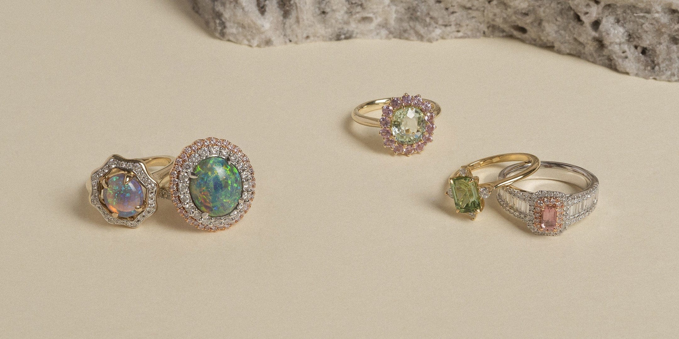 A collection of opal and tourmaline rings displayed on a cream background.