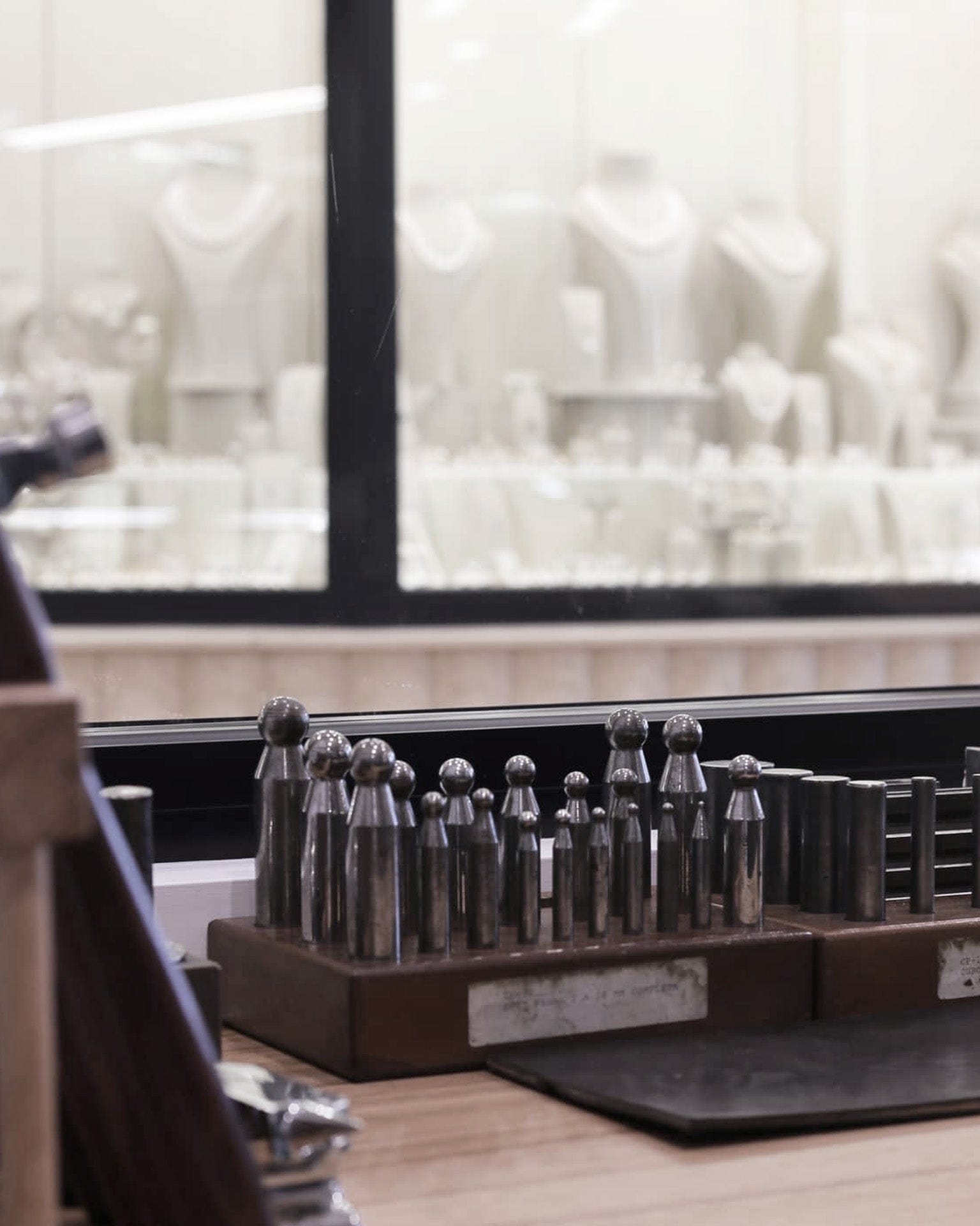 Jewellery forming tools on jewellery workshop bench with showroom display cabinets blurred in background.