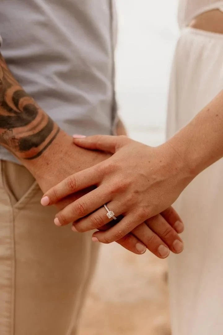 Woman holding man's hand, wearing an emerald cut solitaire diamond ring, following their proposal.