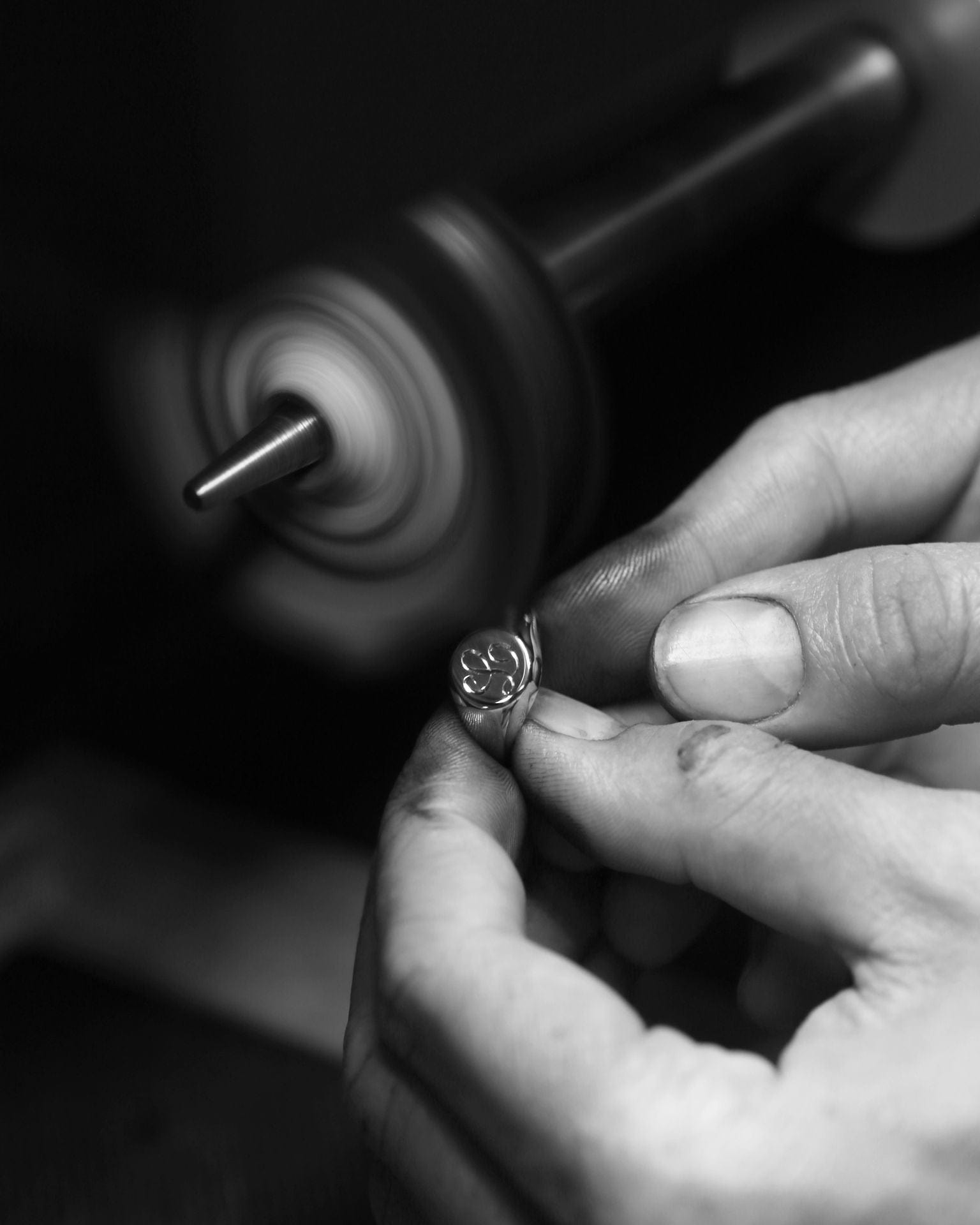 Jeweller holding engraved signet ring at polishing wheel.