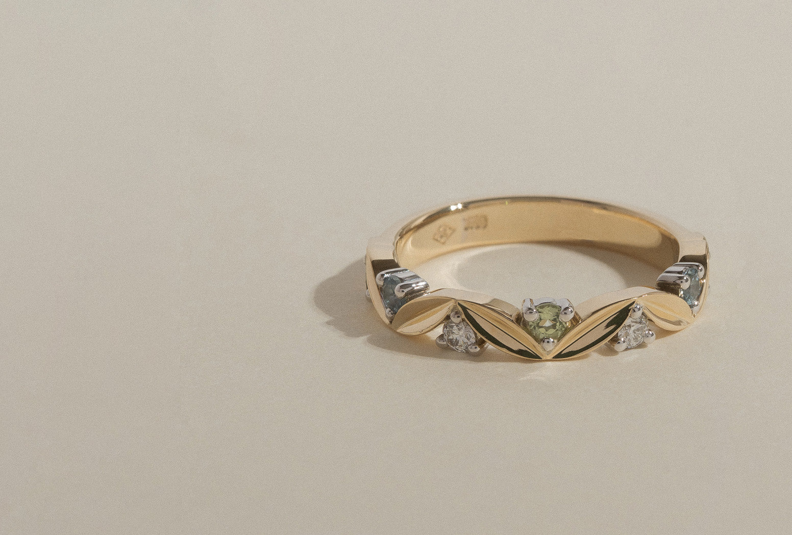 18k yellow and white gold band with leaf shaped motifs, set with round brilliant cut natural white diamonds, peridot, and aquamarine. 