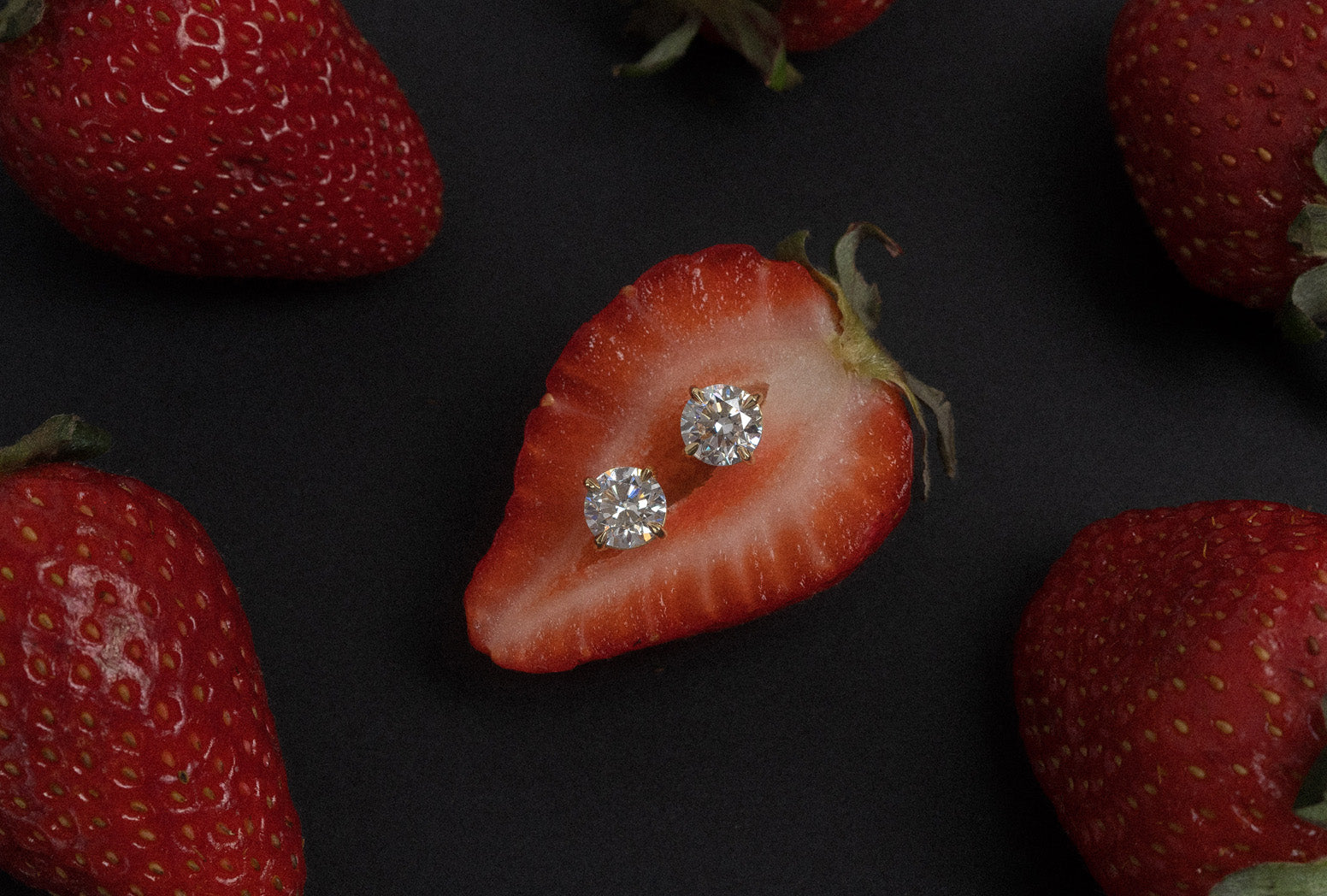Cut strawberry with 1.00ct round brilliant cut white diamond stud earrings on a black background.