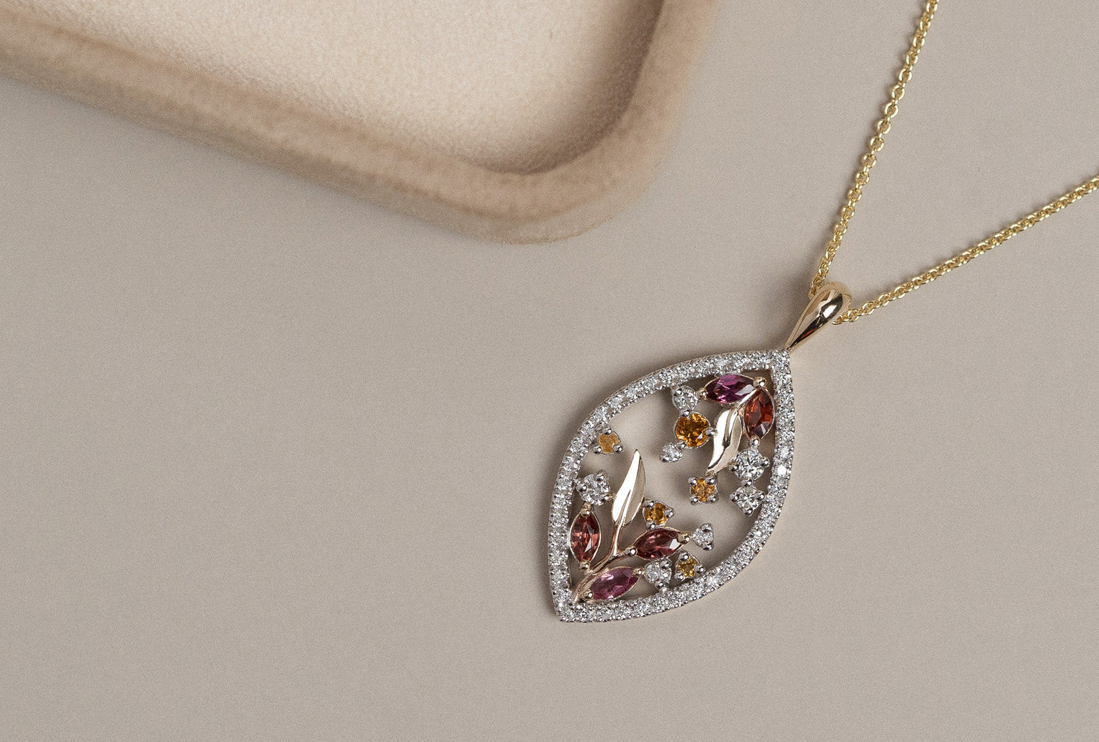 Yellow and white gold garnet, citrine, and diamond cluster pendant on a cream background.