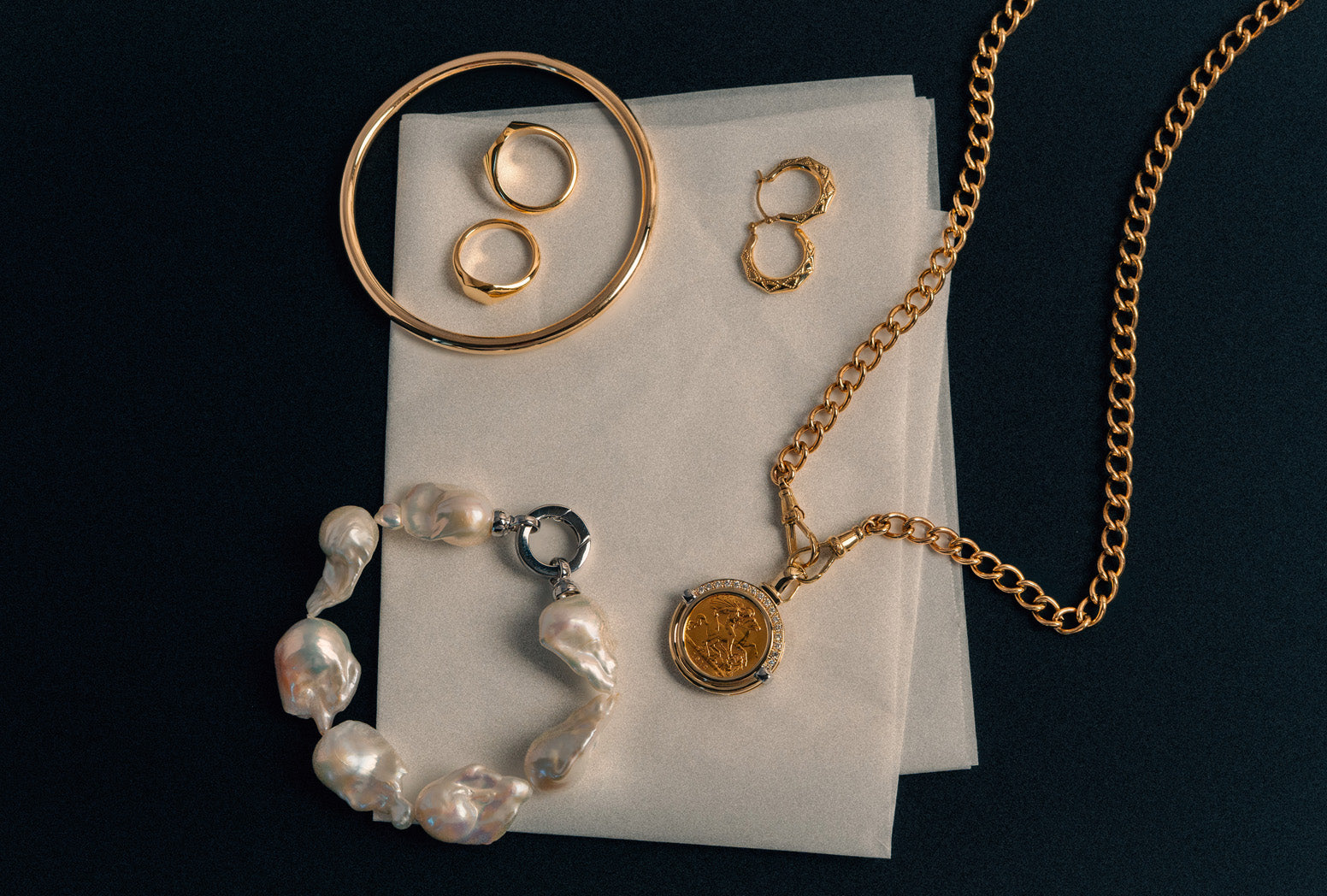 Collation of Mothers Day gifting: gold bangle, gold signet rings, gold hoop earrings, gold curb chain with sovereign pendant and baroque pearl bracelet.