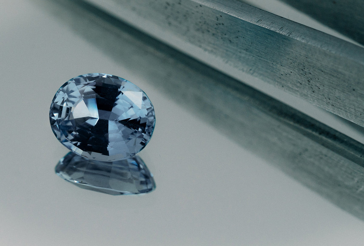 Loose blue oval cut Ceylon sapphire gemstone on mirror background.