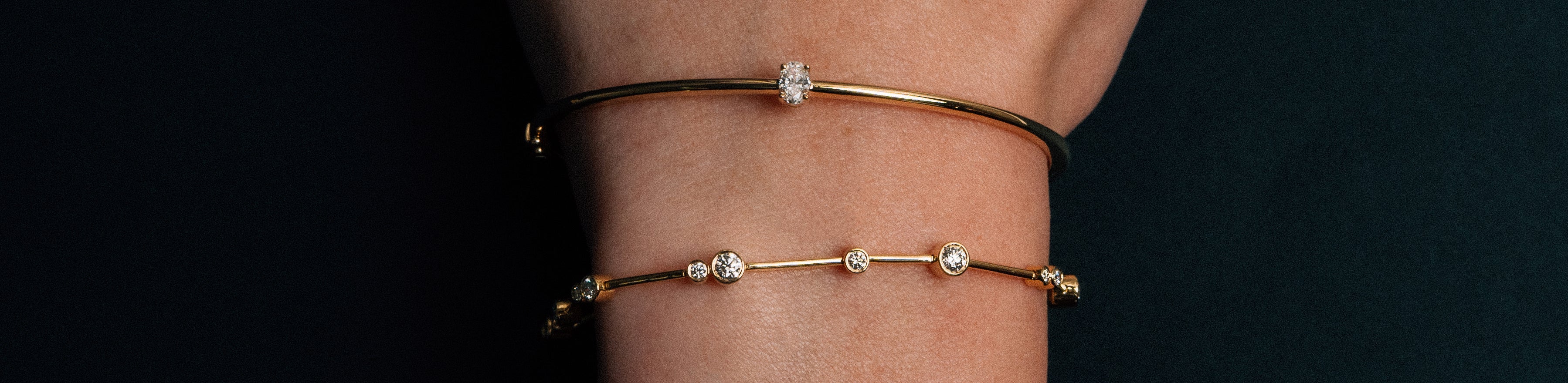 Round brilliant cut diamond bezel set bracelet and an oval cut diamond hinged bangle on a model with a black background. 