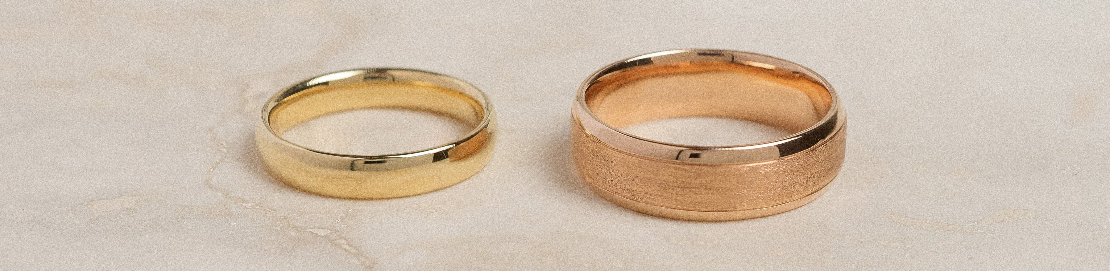 A yellow gold and rose gold plain wedding band on a travertine tile