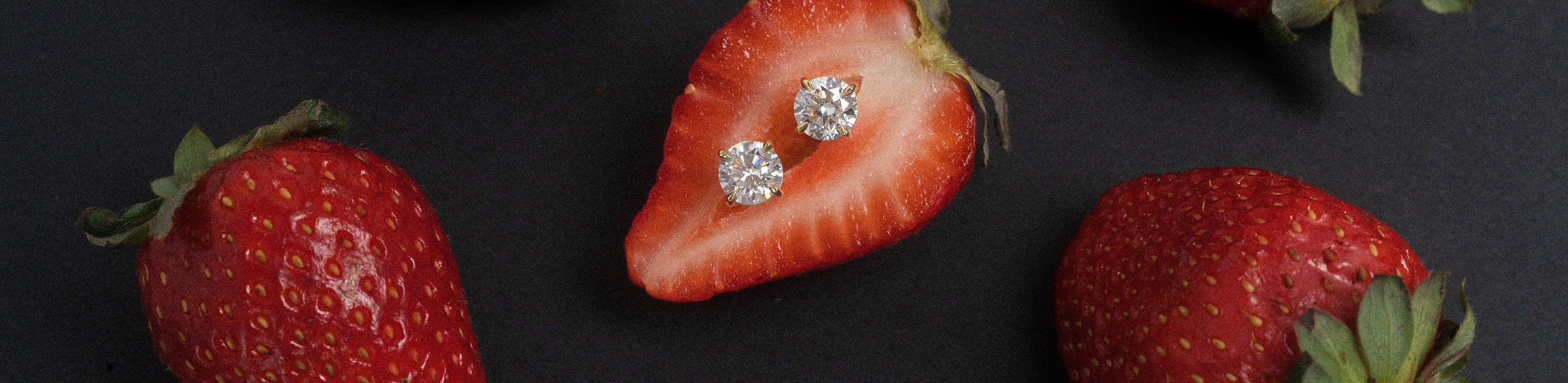 Natural white diamond stud earrings positioned in a strawberry on black background.