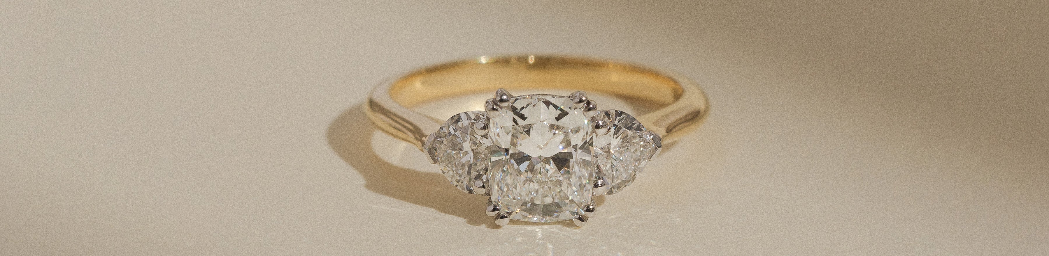 Cushion cut trilogy ring on a cream background