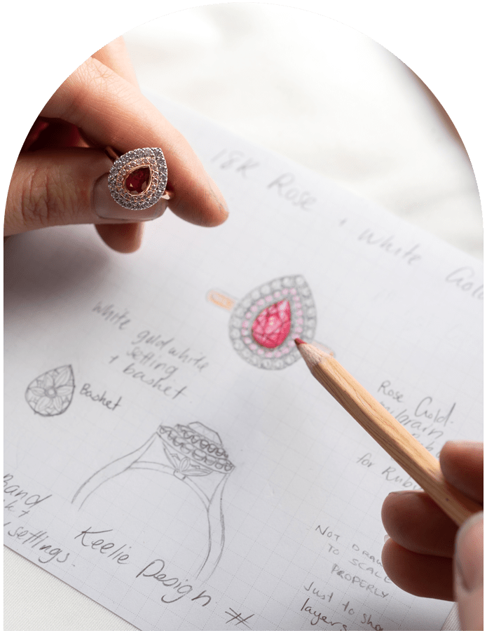 Jewellery designer's hand holding a ruby and diamond ring, whilst sketching a bespoke piece.