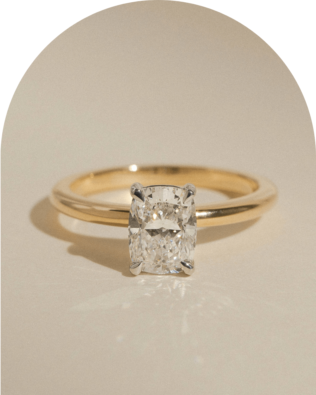 Yellow and white gold solitaire elongated cushion cut diamond ring on beige background.