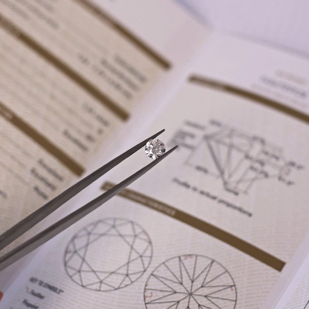 Tweezers holding round brilliant cut white diamond above GIA diamond certificate.
