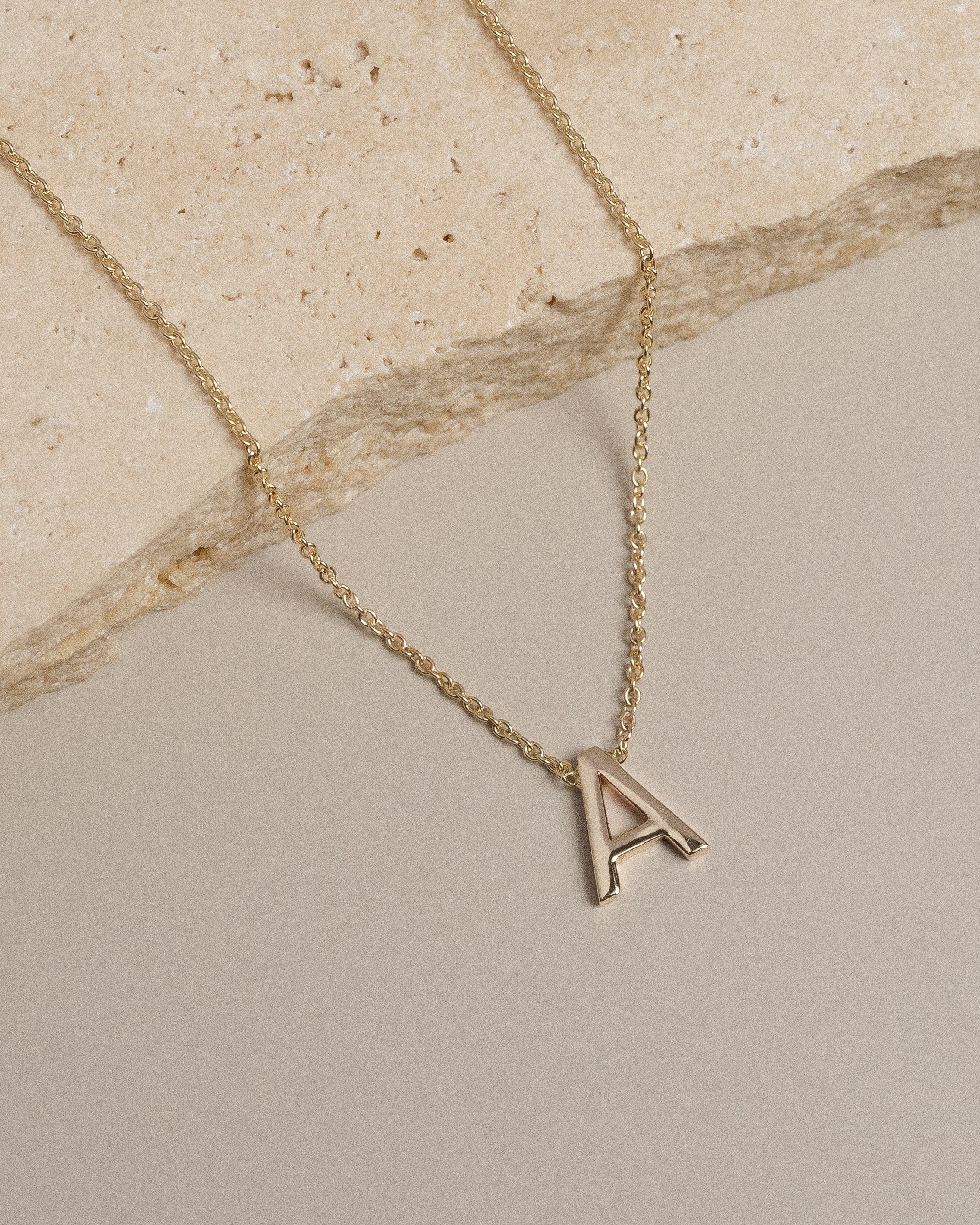 Yellow gold necklace with petite A initial on travertine and beige background.