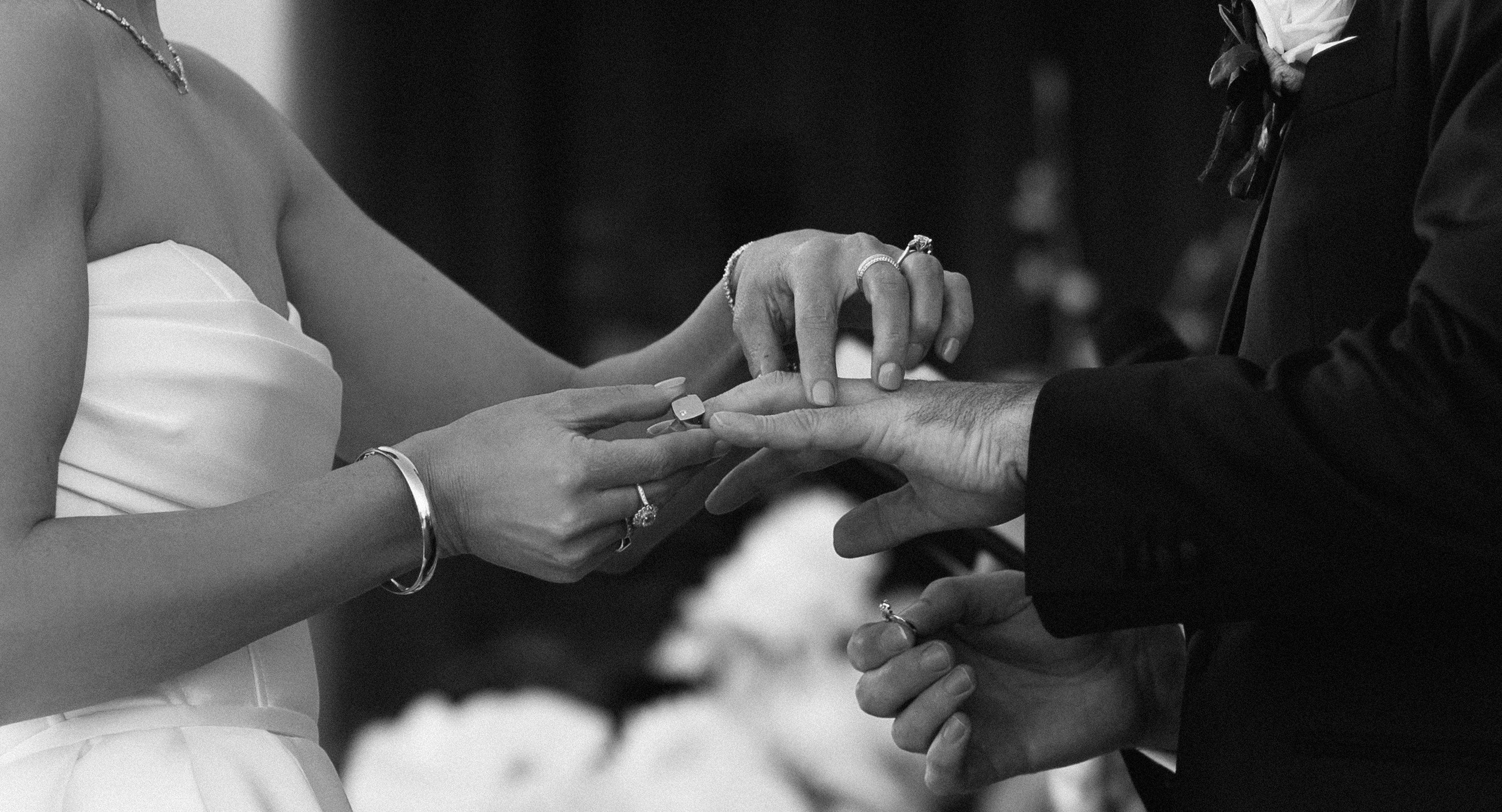 Bride sliding gents wedding ring onto groom's hand, as groom holds bride's wedding ring.