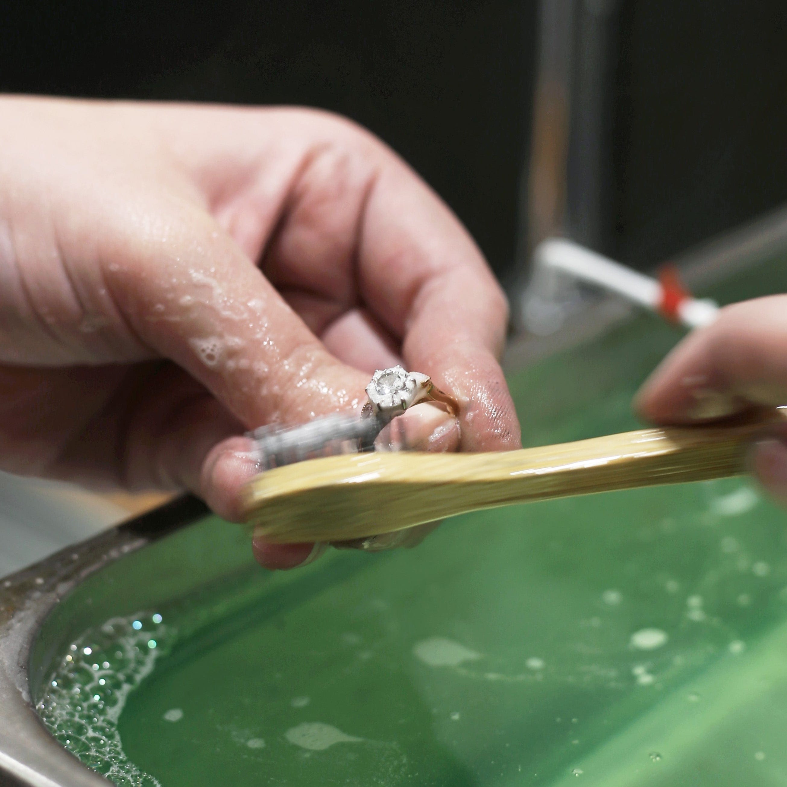 Jeweller using a brush to clean diamond ring above ultrasonic machine.