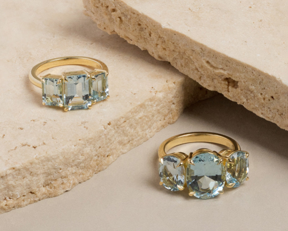 Two variations of aquamarine trilogy rings positioned on travertine