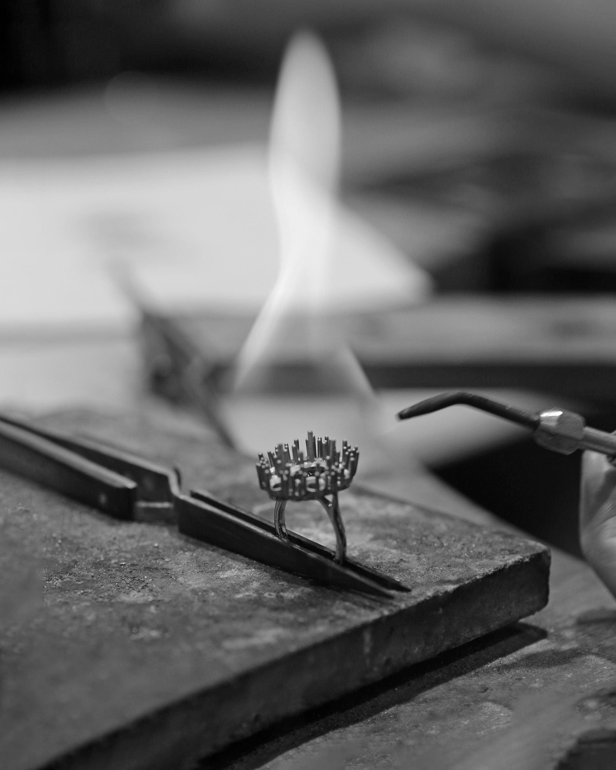 Tweezers holding cluster ring setting on jewellery bench while it is soldered using solder torch.